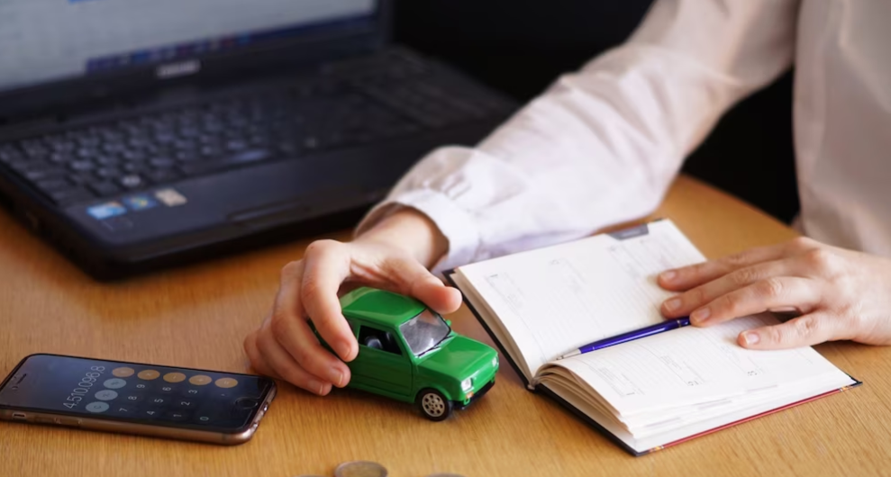 Ejecutivo con una libreta, calculadora, computador y un auto de juguete sobre su escritorio